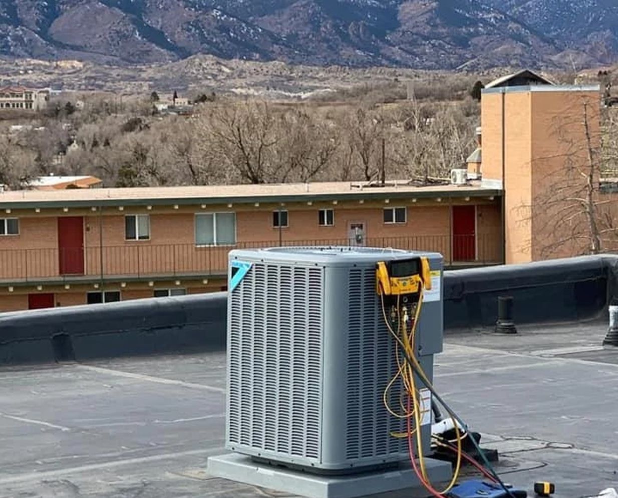 A rooftop air conditioning unit on a service call in Colorado Springs, gauges connected, with Pikes Peak behind it